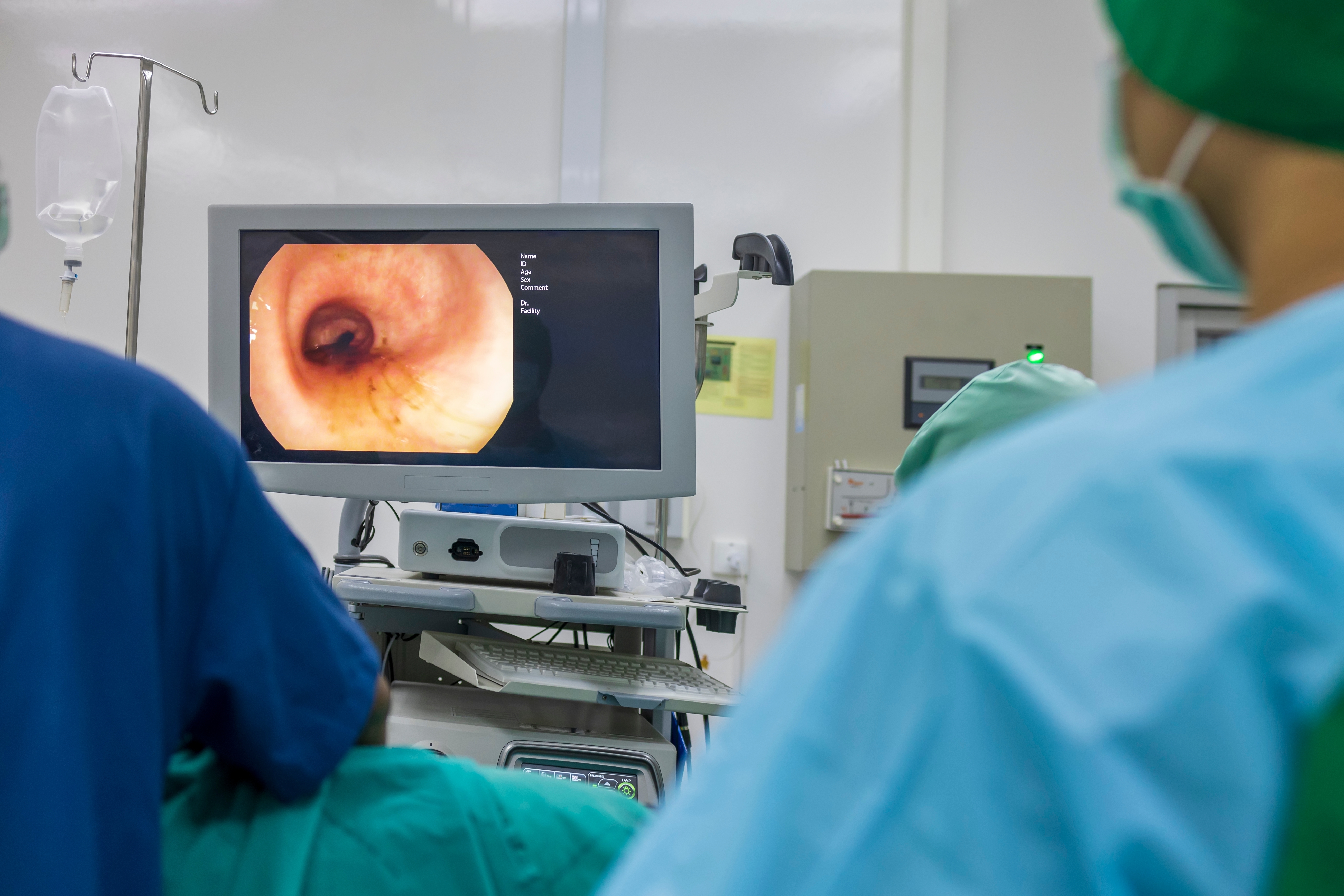 Medical professional in a light blue protective gown performing a colonoscopy procedure in a clinical operating theatre.