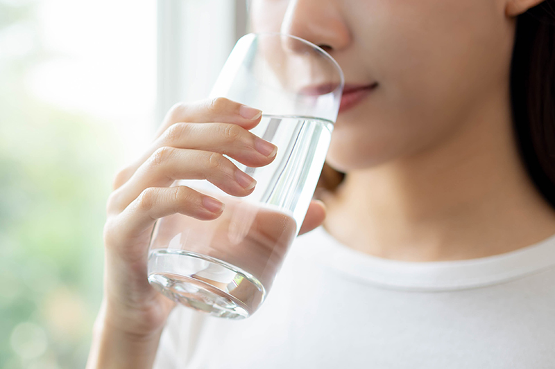 Asian woman smiling and drinking a glass of water representing health, hydration and a healthy lifestyle.