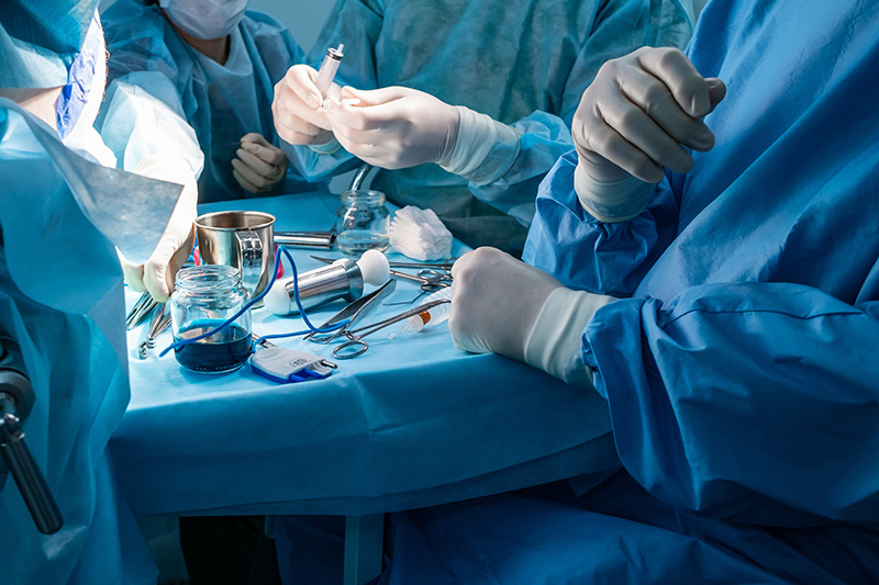 Group of surgeons in sterile surgical gowns and masks performing a minimally invasive surgery with medical instruments in an operating theatre.